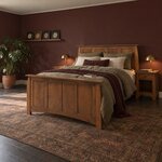 Diagonal angled room view showing the left side of a Craftsman panel bed with a four-panel footboard, in a burgundy bedroom.