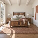 Front room view of a farmhouse panel bed with chunky square posts, in a white plaster bedroom with a beamed ceiling.