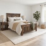 Diagonal angled room view showing the right side of a farmhouse panel bed with a plank footboard, in a bright white bedroom.