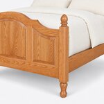 Footboard close-up of a traditional panel bed, showing an arched raised panel, an acorn-finial square post and a turned foot.