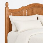 Headboard close-up of a traditional panel bed, showing the arched crest rail, raised panels and an acorn-finial square post.