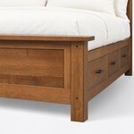 Footboard close-up of a platform storage bed, showing the overhanging cap rail, a pegged square post and metal bar pulls.