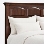 Headboard close-up of a traditional panel bed, showing arched raised panels under rope molding and a stepped crown.