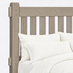 Headboard close-up of a rustic slat bed, showing a chamfered post top, a pegged through-tenon and flat vertical slats.