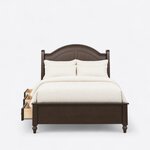 Front view of a traditional storage bed, showing an arched two-panel headboard, a low solid footboard and turned foot legs.