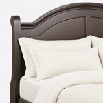 Headboard close-up of a traditional storage bed, showing the molded arched crest, a scroll-topped post and recessed panels.