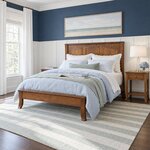 Diagonal angled room view showing the left side of a Shaker panel bed with a low footboard, in a navy wainscoted bedroom.