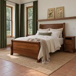 Diagonal angled room view showing the left side of a traditional sleigh bed with scrolled posts, in a tile-floored bedroom.