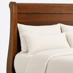 Headboard close-up of a traditional sleigh bed, showing the rolled top rail, a scroll-topped post and horizontal planks.