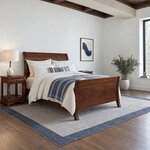 Diagonal angled room view showing the right side of a modern sleigh bed with flared legs, in a beamed-ceiling bedroom.