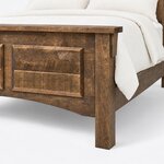 Footboard close-up of a rustic panel bed, showing the cap rail, a corbel bracket, an arched lower rail and a square leg.