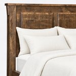 Headboard close-up of a rustic panel bed, showing raised beveled panels, a corbel bracket and an overhanging cap rail.