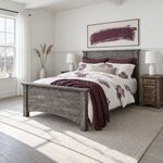 Diagonal angled room view showing the left side of a rustic panel bed with a plank footboard, in a white farmhouse bedroom.