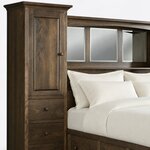 Headboard close-up of a wall unit storage bed, showing a raised-panel tower door, knobbed drawers and beveled mirrors.