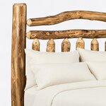 Headboard close-up of a rustic log bed, showing a tall log post, an arched branch crest and pointed log pickets below a rail.