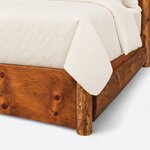 Footboard close-up of a rustic bookcase bed, showing a round log post, a solid low footboard and a half-log side rail.