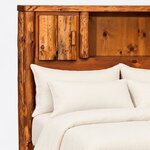 Headboard close-up of a rustic bookcase bed, showing a planked cabinet door with a block pull, a log divider and a cubby.