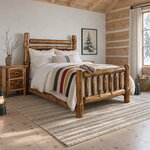 Diagonal angled room view showing the right side of a rustic log bed with a slatted footboard, in a log cabin bedroom.