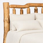Headboard close-up of a rustic log bed, showing the curving top log rail, pointed log spindle tops and a thick log post.
