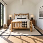 Front room view of a rustic log bed with a curving log headboard rail, in a white vaulted bedroom with plank walls.