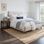 Diagonal angled room view showing the right side of a contemporary upholstered bed with nailhead trim, in a white bedroom.