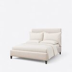 Diagonal angled view showing the left side of a contemporary upholstered bed, with nailhead trim and a low footboard.