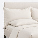 Headboard close-up of a contemporary upholstered bed, showing smooth upholstery with spaced nailheads down the side edge.