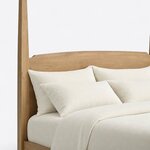 Headboard close-up of a classic pencil post bed, showing a crowned solid panel with notched shoulders beside a faceted post.