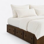 Head end close-up of a minimalist platform bed, showing the squared frame corner and three side drawers with round knobs.