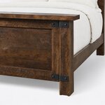 Footboard close-up of an industrial panel bed, showing the overhanging cap, a square corner post and metal corner straps.