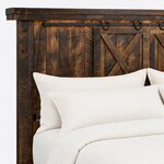 Headboard close-up of a rustic panel bed, showing a stepped cap, a metal barn-door rail with horseshoe hangers and X braces.