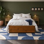 Front room view of a minimalist platform bed with a low solid footboard, in an olive-green bedroom with a picture ledge.