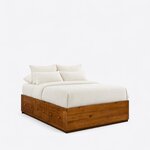 Diagonal angled view showing the right side of a minimalist platform bed, with three knobbed side drawers and no headboard.