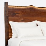 Headboard close-up of a live edge panel bed, showing the undulating live-edge crest, wide slab boards and a block post.