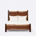 Front view of a live edge panel bed, showing a tall slab headboard with a wavy crest over a low curved footboard.