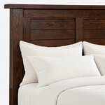 Headboard close-up of a rustic panel bed, showing recessed plank bays split by a center stile under an overhanging cap.