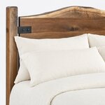 Headboard close-up of a live edge panel bed, showing the wavy crown and a bolted metal strap tying the slab to its post.