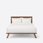 Front view of a contemporary platform bed, showing a wide postless panel headboard above a thin frame on splayed legs.