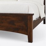 Footboard close-up of a classic panel bed, showing the overhanging cap, the arched lower edge and a tapered square leg.