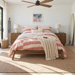 Front room view of a mid-century platform bed with no headboard, in a beach house bedroom with a ceiling fan.