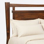 Headboard close-up of a modern panel bed, showing the bowed top rail, an open slot and a projecting cap over a flat panel.