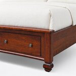 Footboard close-up of a classic storage bed, showing the rounded cap rail, a faceted bun foot and round drawer knobs.