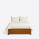 Front view of a modern platform bed, showing a low solid footboard with a routed line between square block legs.