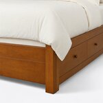 Footboard close-up of a modern platform bed, showing a square block leg, the low grooved footboard and round drawer knobs.