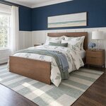 Diagonal angled room view showing the left side of a modern panel bed with a slab footboard, in a navy wainscoted bedroom.