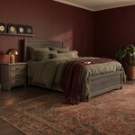 Diagonal angled room view showing the right side of a rustic panel bed with a framed panel headboard, in a burgundy bedroom.
