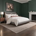 Diagonal angled room view showing the right side of a modern upholstered bed with channel tufting, in a green-paneled room.