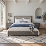 Front room view of a modern upholstered bed with a wood-framed headboard, in a white plaster bedroom with an arched niche.