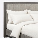 Headboard close-up of a modern upholstered bed, showing the woven-texture upholstered panel set inside a wide wood frame.