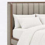 Headboard close-up of a modern upholstered bed, showing vertical channel tufting and a slim top rail curving into the wing.